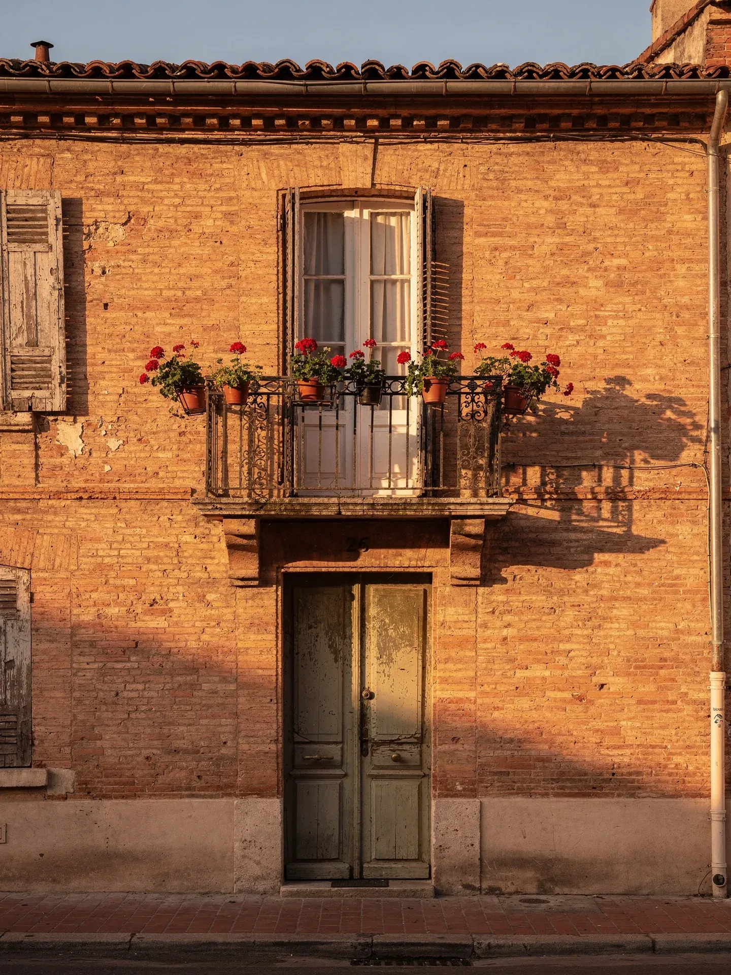 Maison toulousaine traditionnelle en brique foraine avec balcon en fer forgé et géraniums rouges